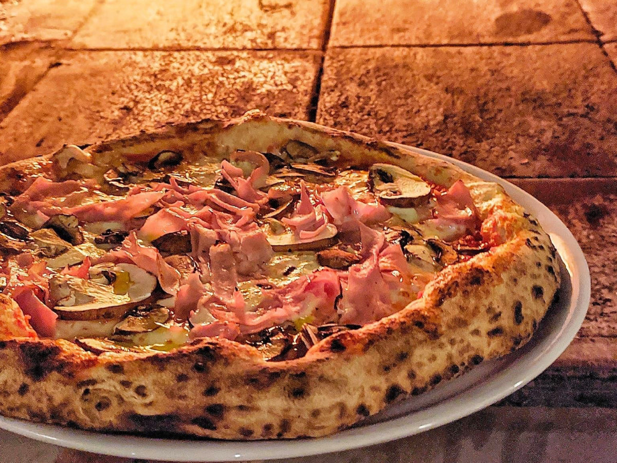A delicious wood-fired pizza with ham and mushrooms by Pizzeria On The Road mobile wood-fired pizza catering.